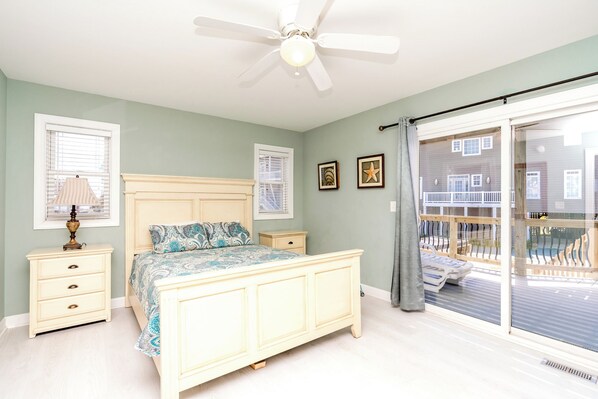 A bedroom with a bed, bedside tables, a ceiling fan, and a sliding glass door to a balcony. - @ THE PEACH offers an escape to an oceanfront/oceanside (Sneads Ferry)