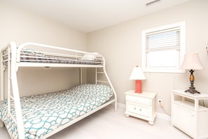 Una cama litera con un colchón estampado, una mesita de noche con lámpara y una ventana con persianas.