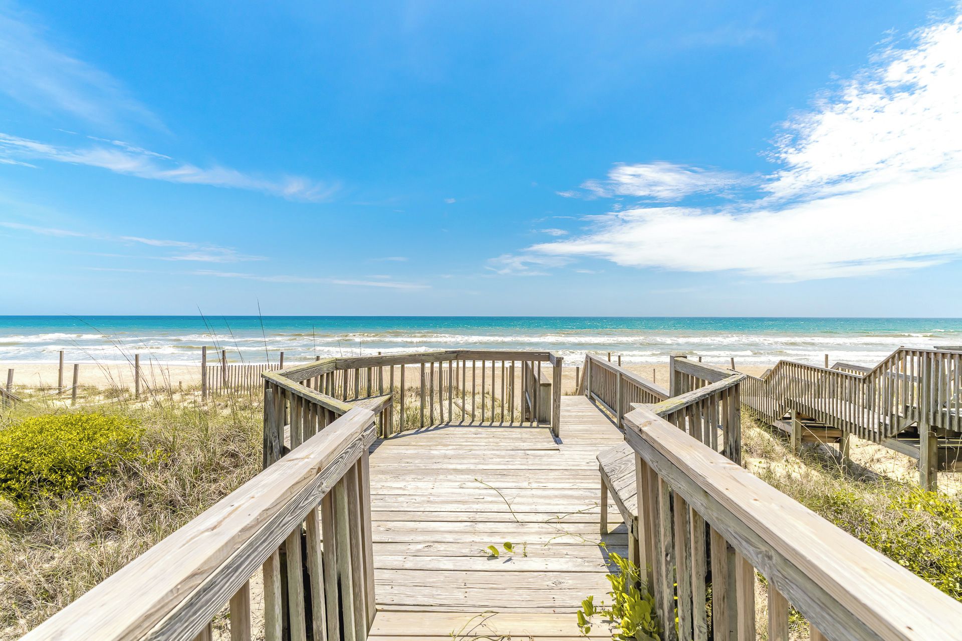 A wooden boardwalk leading to a beach with a clear sky.