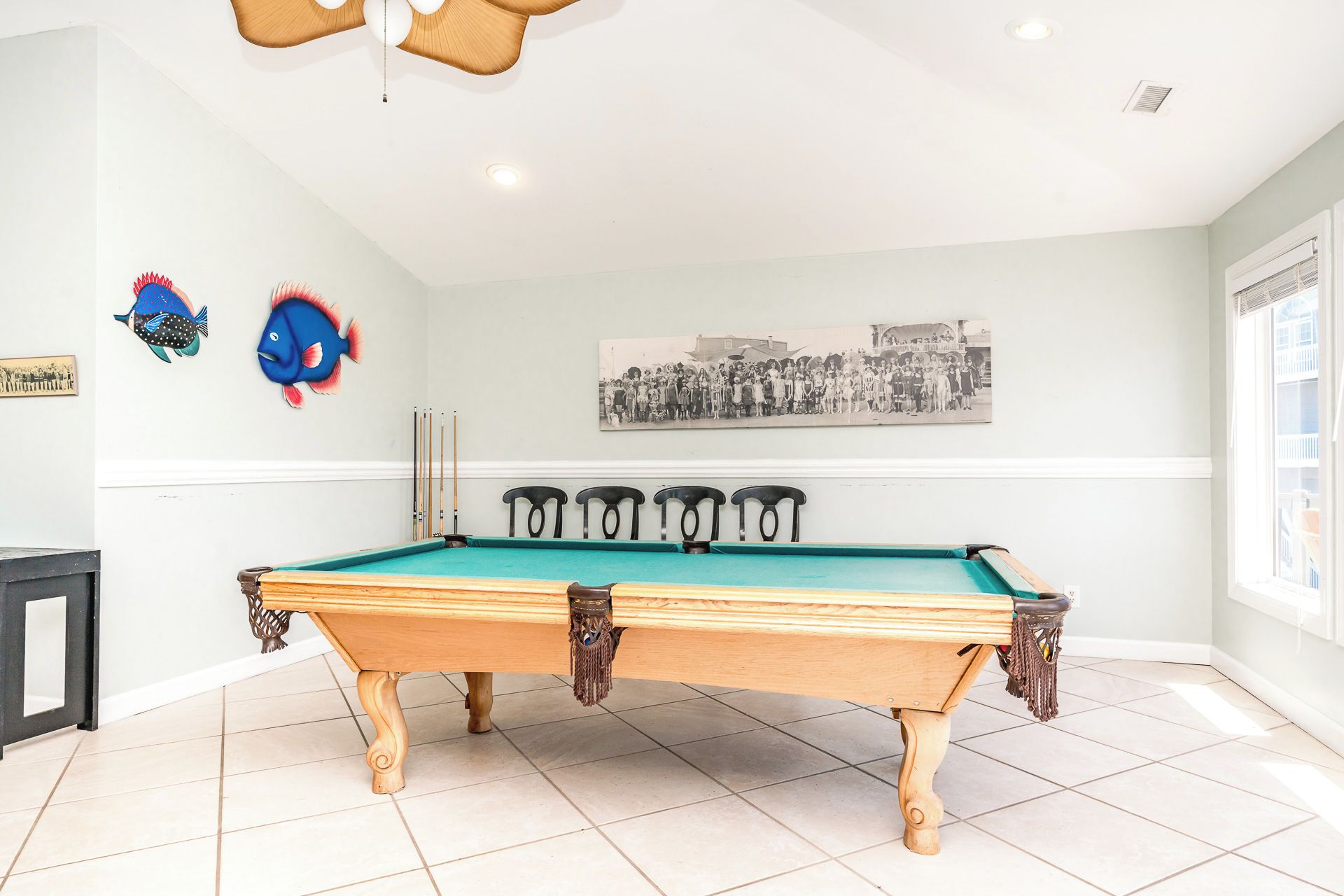 A pool table with four chairs, a ceiling light fixture, and a wall-mounted photograph.