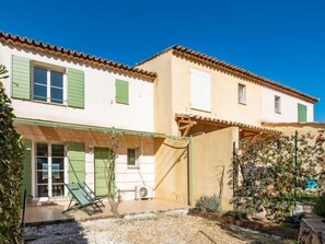 Una casa de dos pisos con un patio cubierto, un pequeño jardín y una piscina.