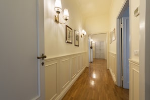 A hallway with wooden flooring, white wainscoting, and wall-mounted light fixtures. - Luxury Signoria by Mmega (Florence)