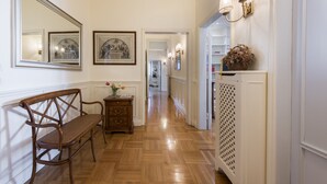 A hallway with wooden flooring, a bench, a dresser, framed pictures, and wall sconces.