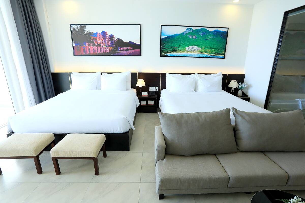 Quarto de hotel com duas camas, um sofá e duas mesas de cabeceira com luminárias.