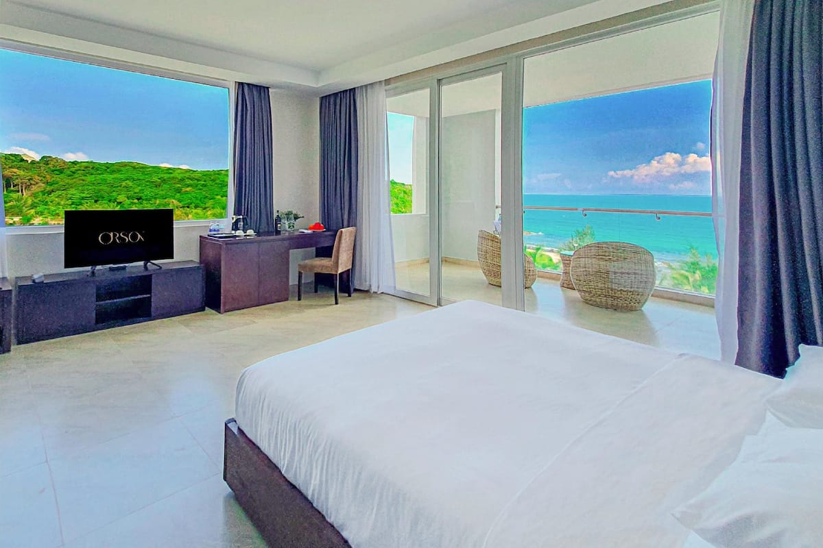 Quarto de hotel com cama, escrivaninha e televisão, e vista para o oceano.