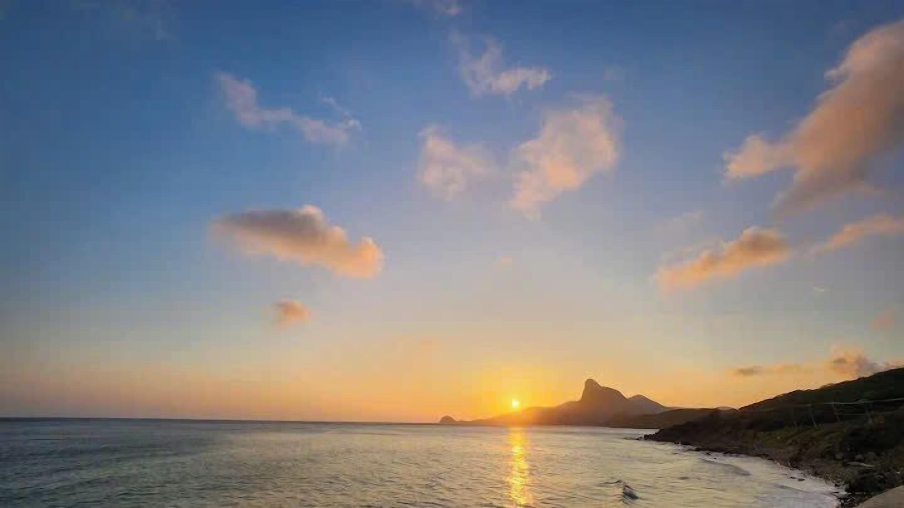 Un atardecer costero con aguas tranquilas reflejando el cielo.