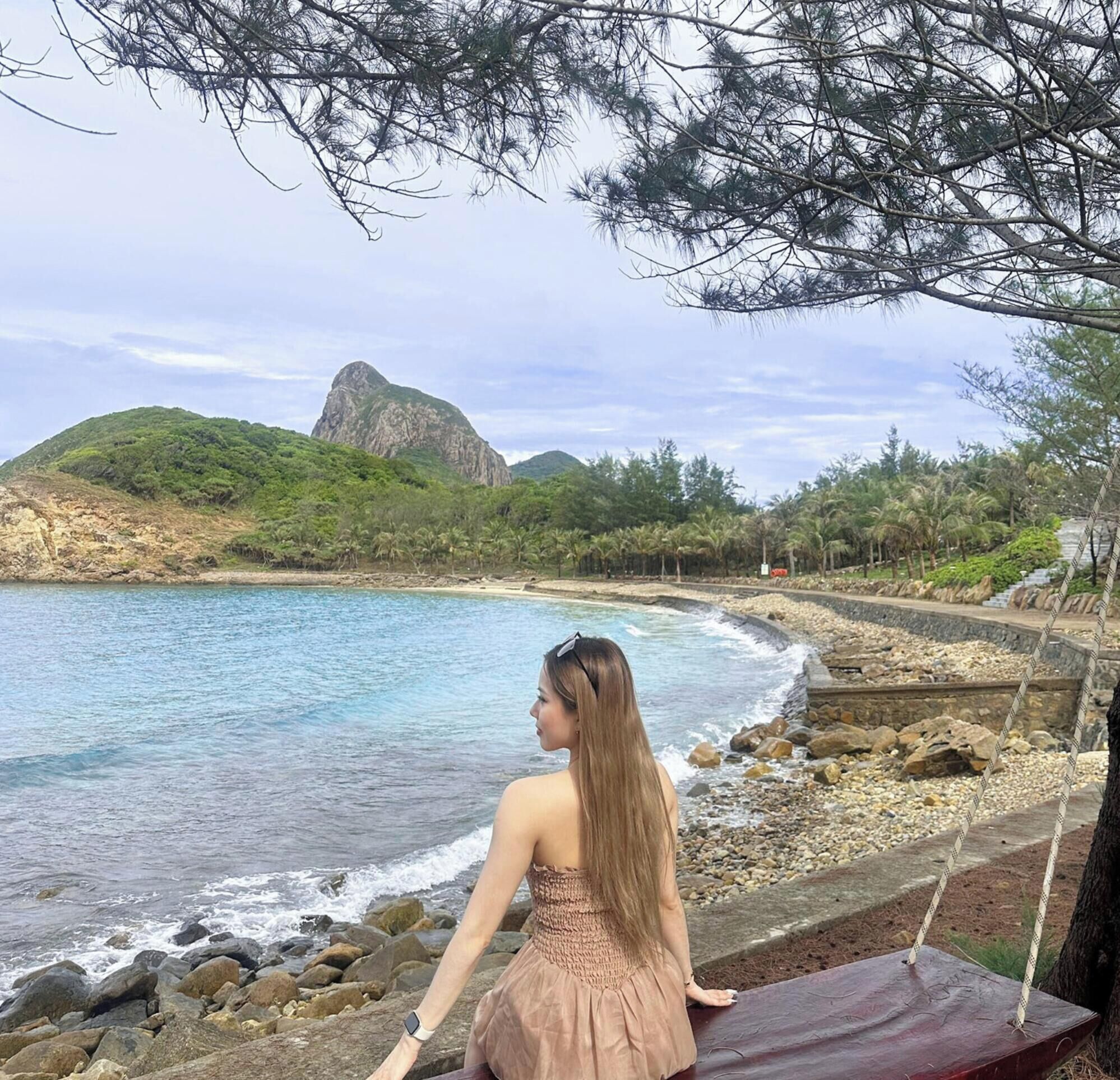 A coastal view with a rocky shoreline, a clear blue sea, and a large mountain in the background.
