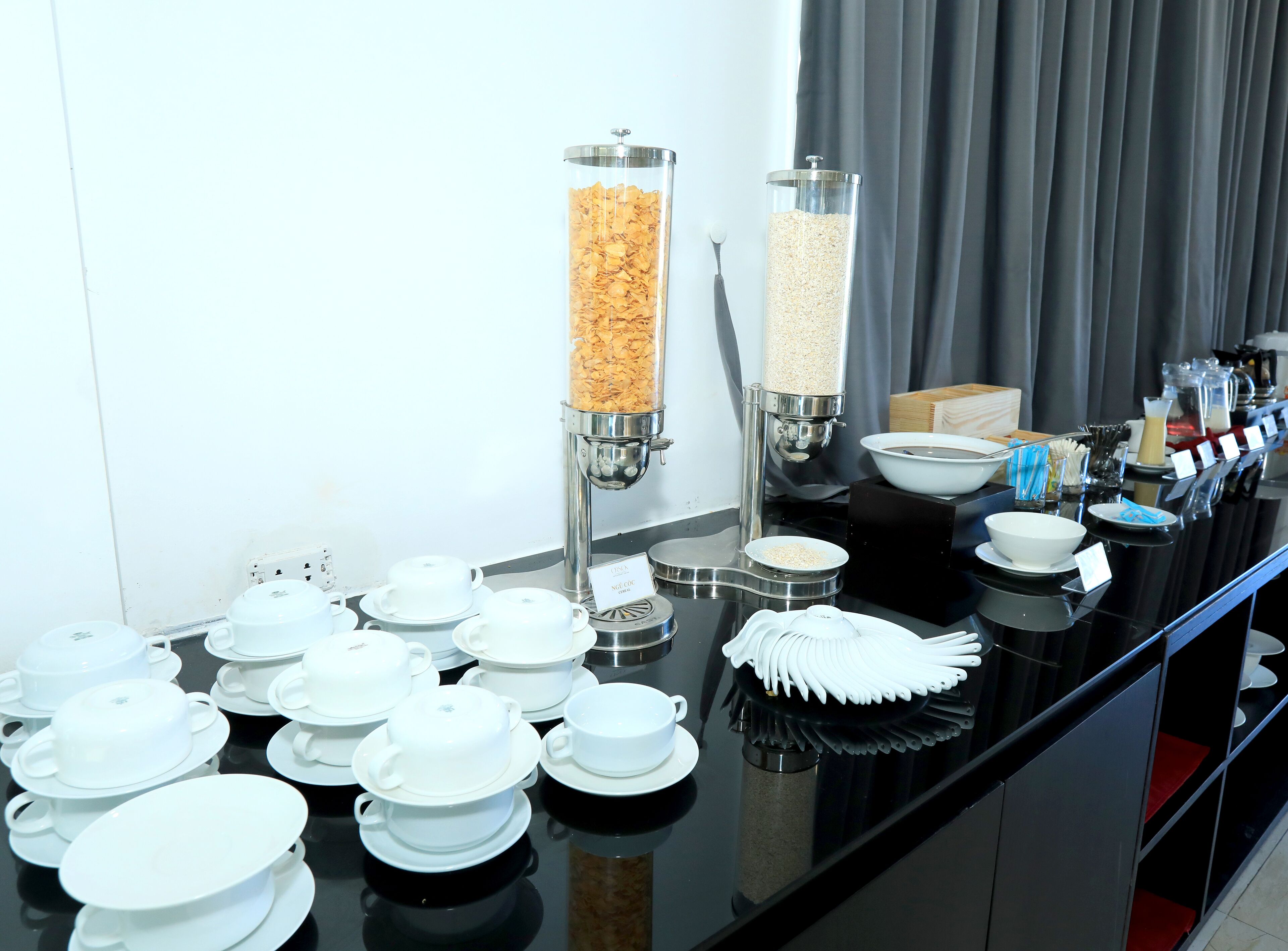 Un buffet avec différents bols et tasses, une machine à café et un distributeur de céréales.