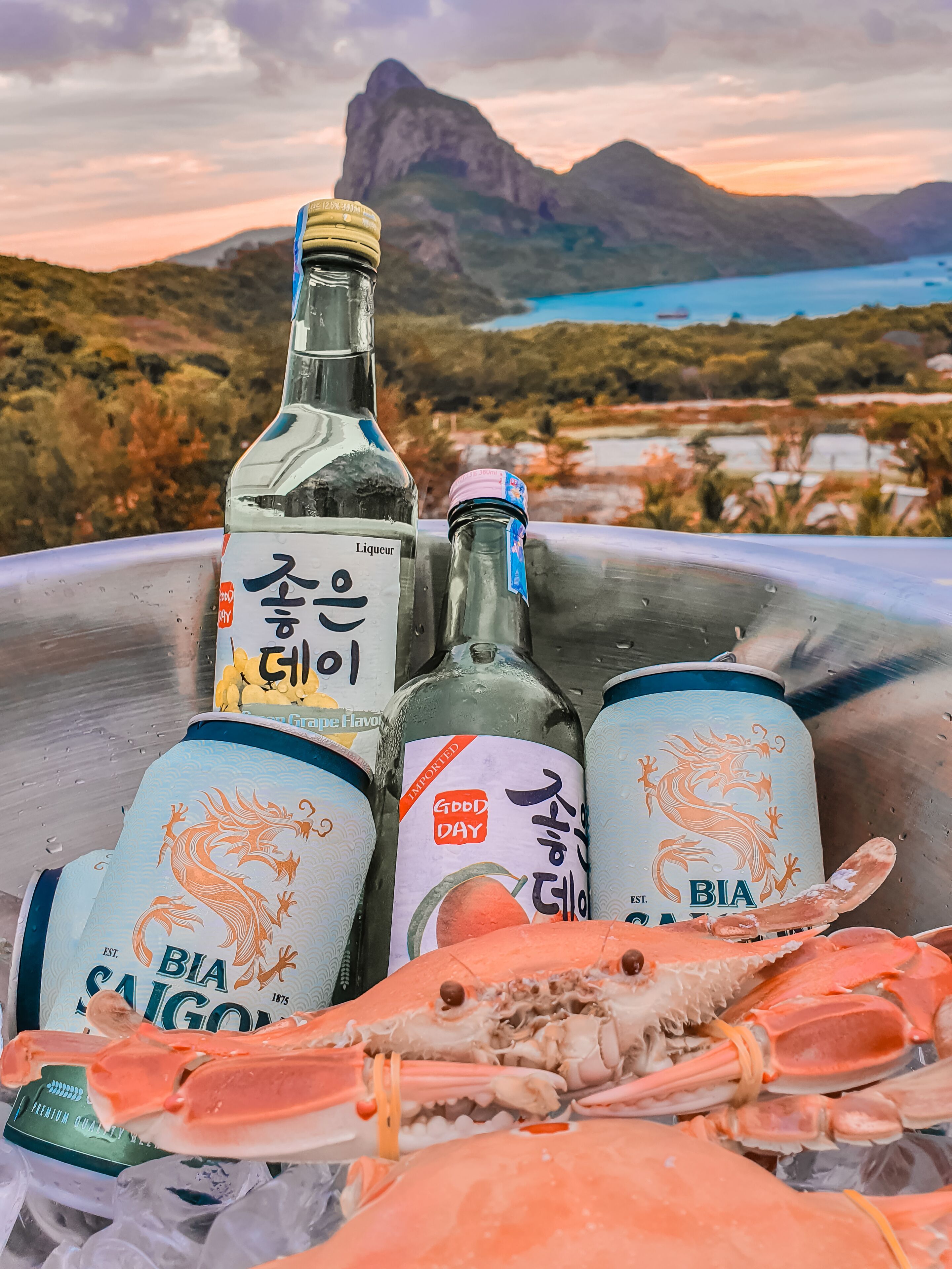 Un recipiente metálico con una botella de licor, dos latas de cerveza BIA Saigon y un cangrejo sobre hielo.