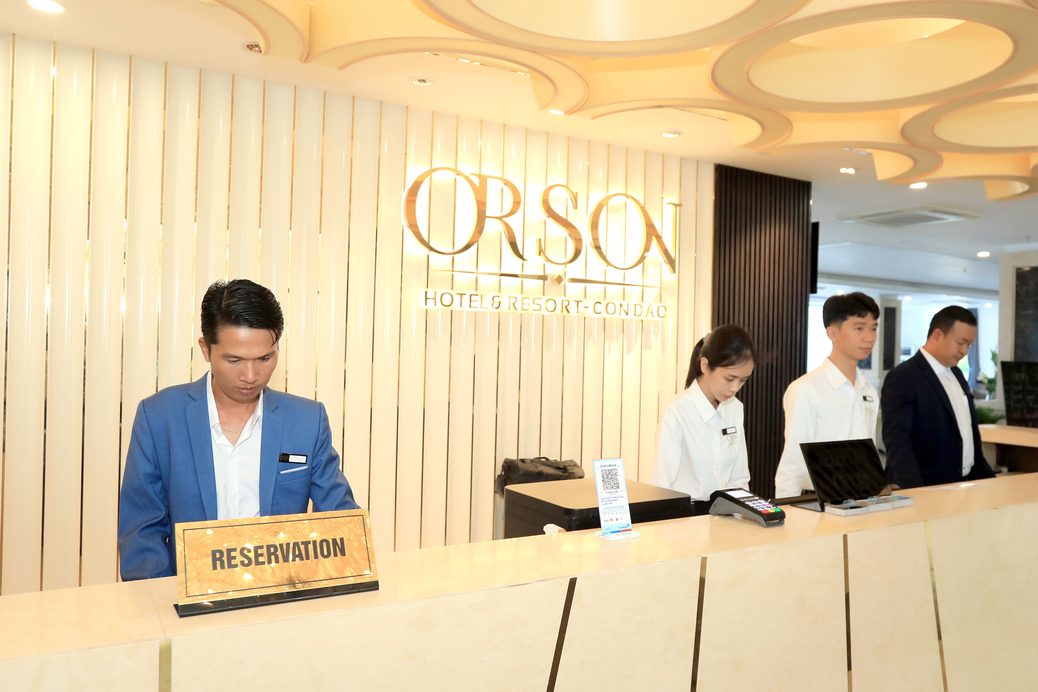 Una reception hotel con un cartello che riporta la scritta 'RESERVATION' e personale che assiste gli ospiti.