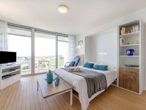 Una habitación de hotel moderna con una cama grande, un televisor, un balcón con vistas y una estantería.