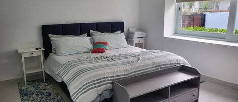 Une chambre à coucher comprenant un lit, des tables de chevet, une fenêtre et un banc intégré.