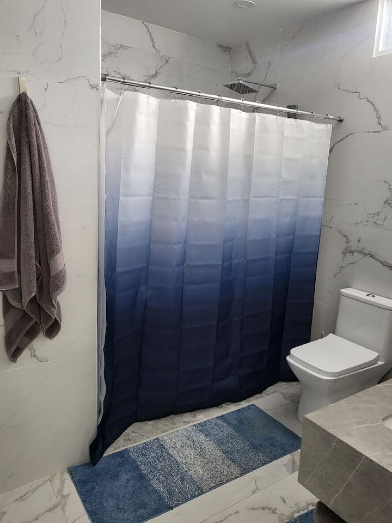 Une salle de bain avec un sol en marbre, des toilettes blanches, un rideau de douche bleu dégradé et une serviette accrochée au mur.