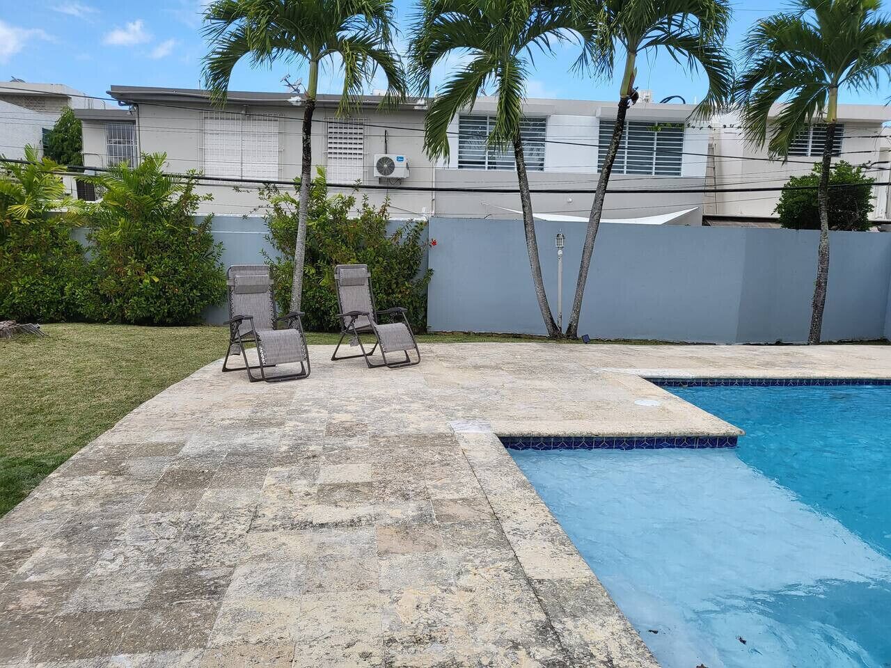 Una piscina con dos sillas reclinables y un césped.