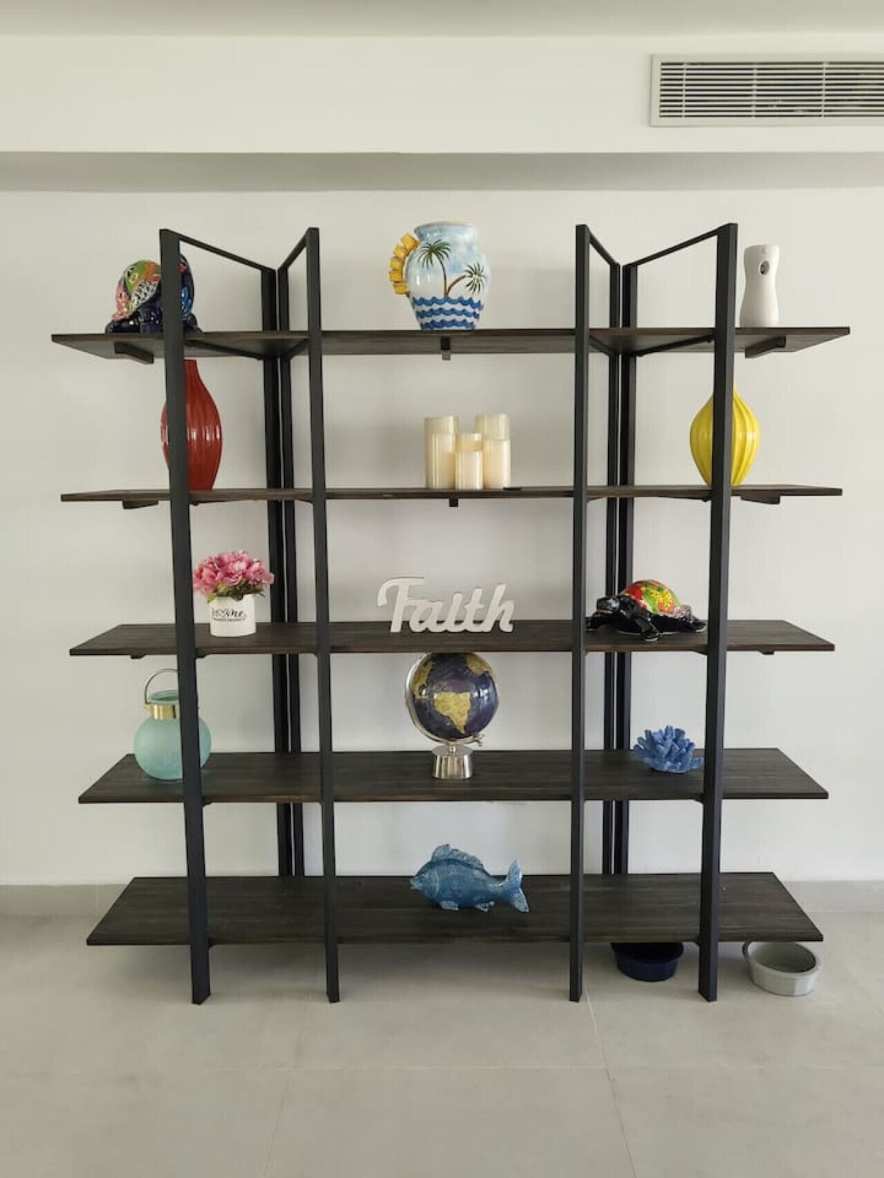 A black metal shelf unit with various decorative items on each shelf, including a globe, a fish sculpture, and a vase.