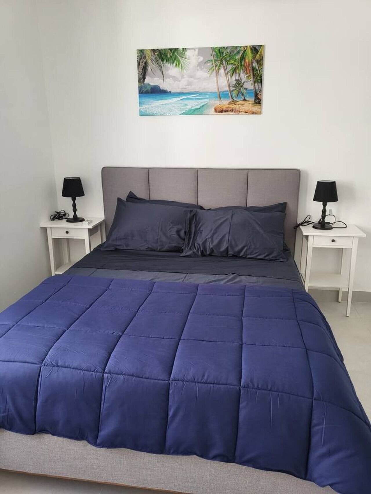A bedroom with a bed, two bedside tables, and a painting of a beach scene.