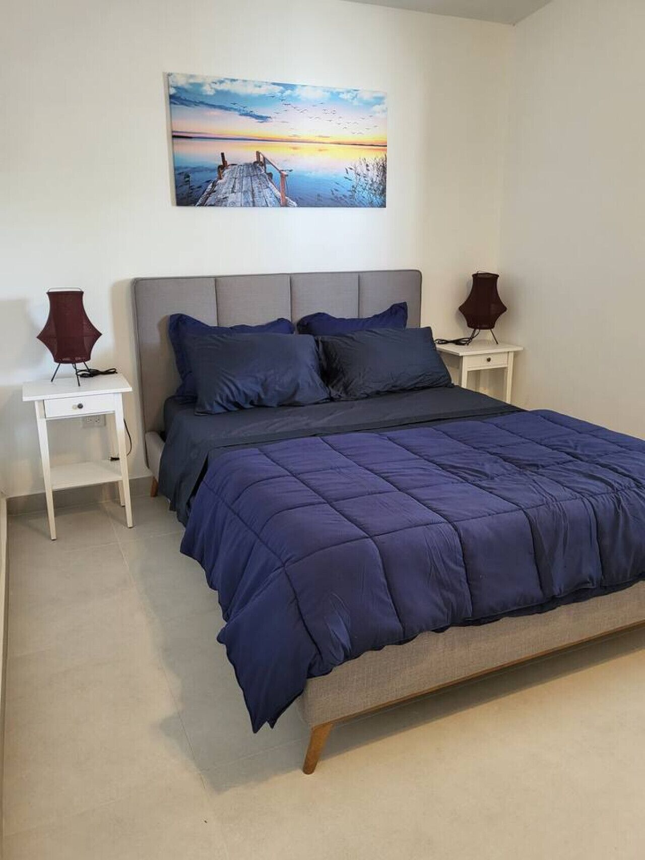 Ein Schlafzimmer mit einem Bett, zwei Nachttischen, einem Wandbild und Blick ins Freie.