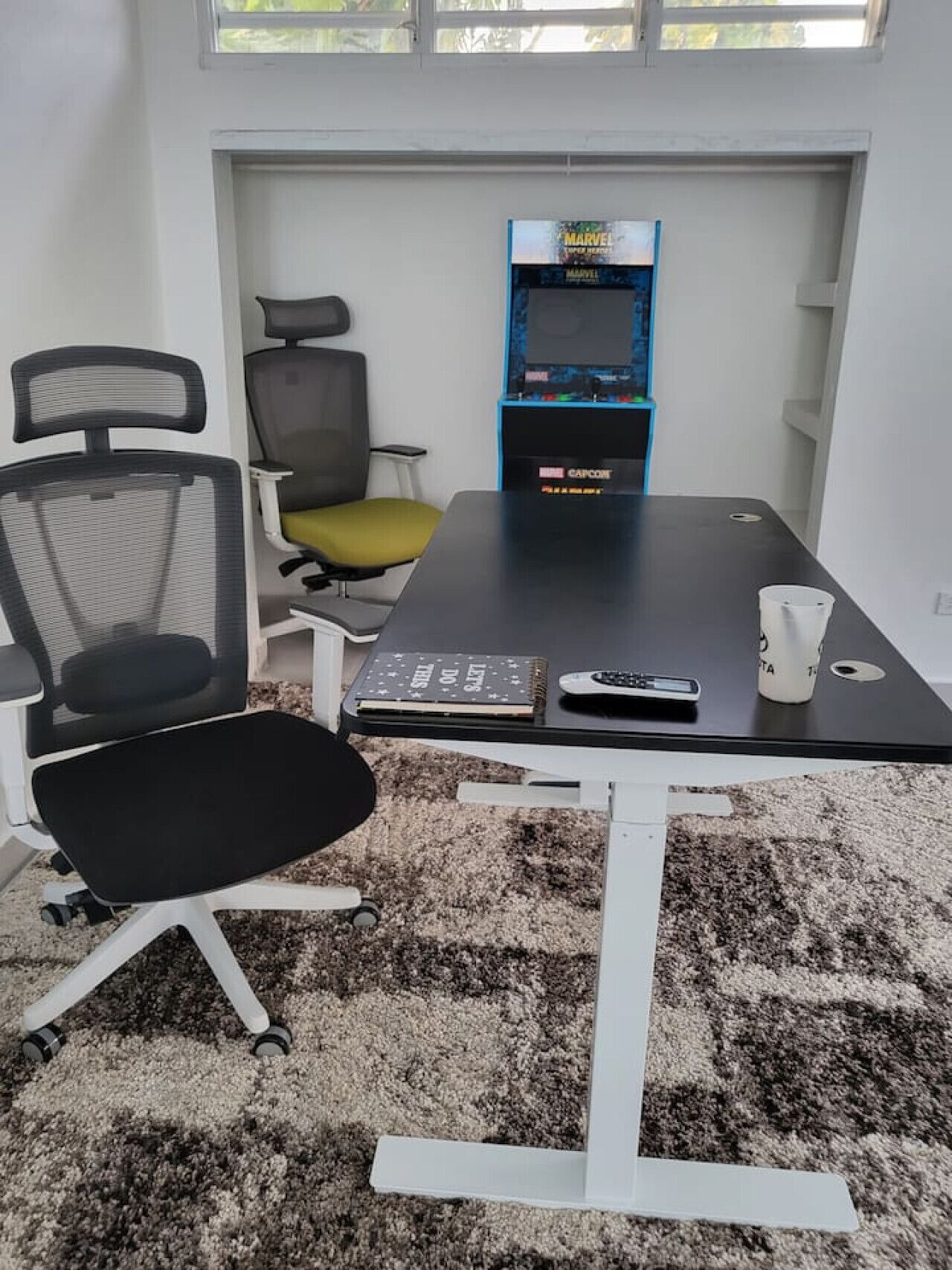 A conference room with a black table, two office chairs, a white coffee cup, and a Marvel-themed arcade machine.