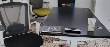 A conference room with a black table, two office chairs, a white coffee cup, and a Marvel-themed arcade machine.