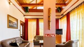 A spacious living room with leather sofas, a wooden TV stand, and a large window with red curtains. - Vacation home Szabo by Interhome (Balatonlelle)