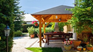 A wooden pergola with a stone pathway leading to a table and chairs, surrounded by potted plants and a well-maintained garden. - Vacation home Szabo by Interhome (Balatonlelle)