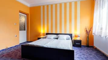 A bedroom with a bed, two bedside tables, a nightstand, a window with curtains, and a wall with vertical stripes.
