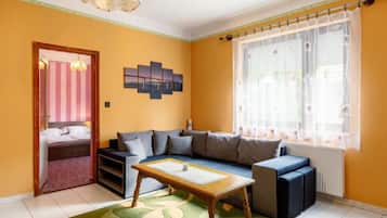 Una sala de estar con un sofá, una mesa de centro de madera, una obra de arte en la pared y una ventana con cortinas.