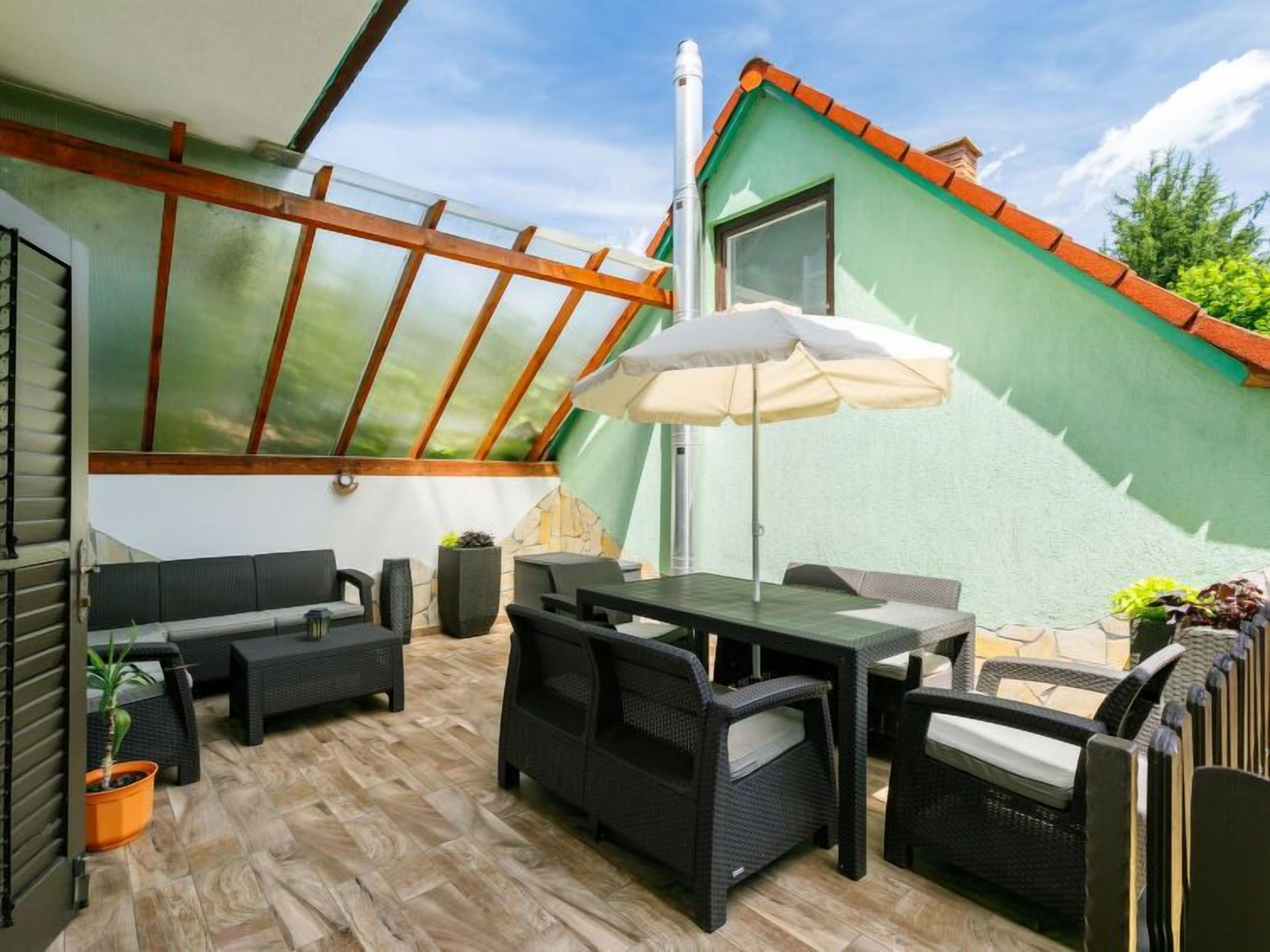 Une terrasse couverte, aménagée avec du mobilier d’extérieur, une table et un grand parasol.