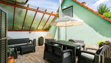 Une terrasse couverte, aménagée avec du mobilier d’extérieur, une table et un grand parasol.