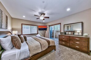 Un dormitorio con cama, cómoda, ventilador de techo y un gran ventanal.