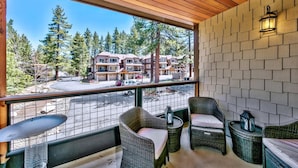 A balcony with wicker furniture, a view of a building complex, and a paved area with cars. - Prime Walk-to-Heavenly Townhome w/ A/C | TW702 (South Lake Tahoe)