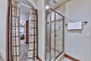 Un baño con cabina de ducha de vidrio, un perchero y un acceso visible a otra habitación.