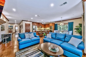 Ein geräumiges Wohnzimmer mit zwei blauen Sofas, einem Couchtisch und einer Küchenzeile im Hintergrund.
