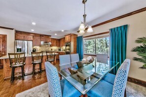 Una cocina moderna con armarios de madera, electrodomésticos de acero inoxidable y un comedor con mesa de vidrio y sillas estampadas.