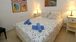 A neatly made bed with floral bedding, two bedside lamps, and four framed artworks on the wall. - Residencial Mar I by Interhome (Alcanar)