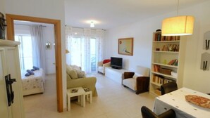 A spacious living area with a sofa, a TV, a bookshelf, and a dining table. - Residencial Mar I by Interhome (Alcanar)