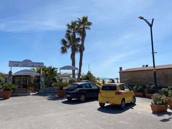 A parking lot with a yellow taxi, a dark-colored car, and a building with a sign for a restaurant and pizzeria.