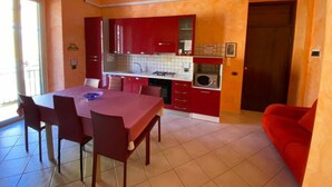 Une cuisine de taille réduite avec des meubles de rangement rouges, une table à manger avec des chaises et un canapé rouge.