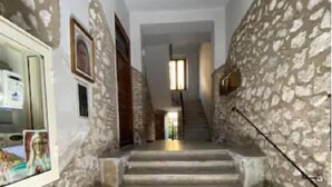 Un couloir aux murs de pierre, avec un escalier menant à un deuxième étage.