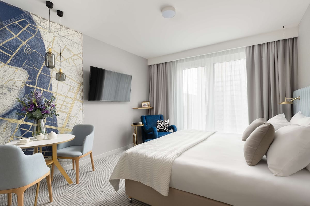 Una habitación de hotel moderna con una cama grande, un escritorio con sillas, un mapa en la pared y un televisor.
