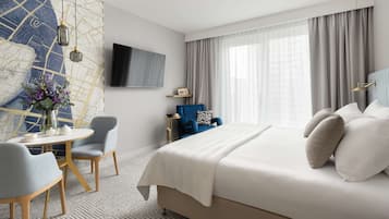A modern hotel room with a large bed, a desk with chairs, a map on the wall, and a television.