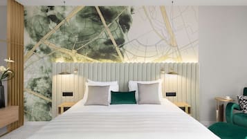 Une chambre moderne avec un grand lit, deux tables de chevet, un fauteuil vert et un mur décoré d’une carte.