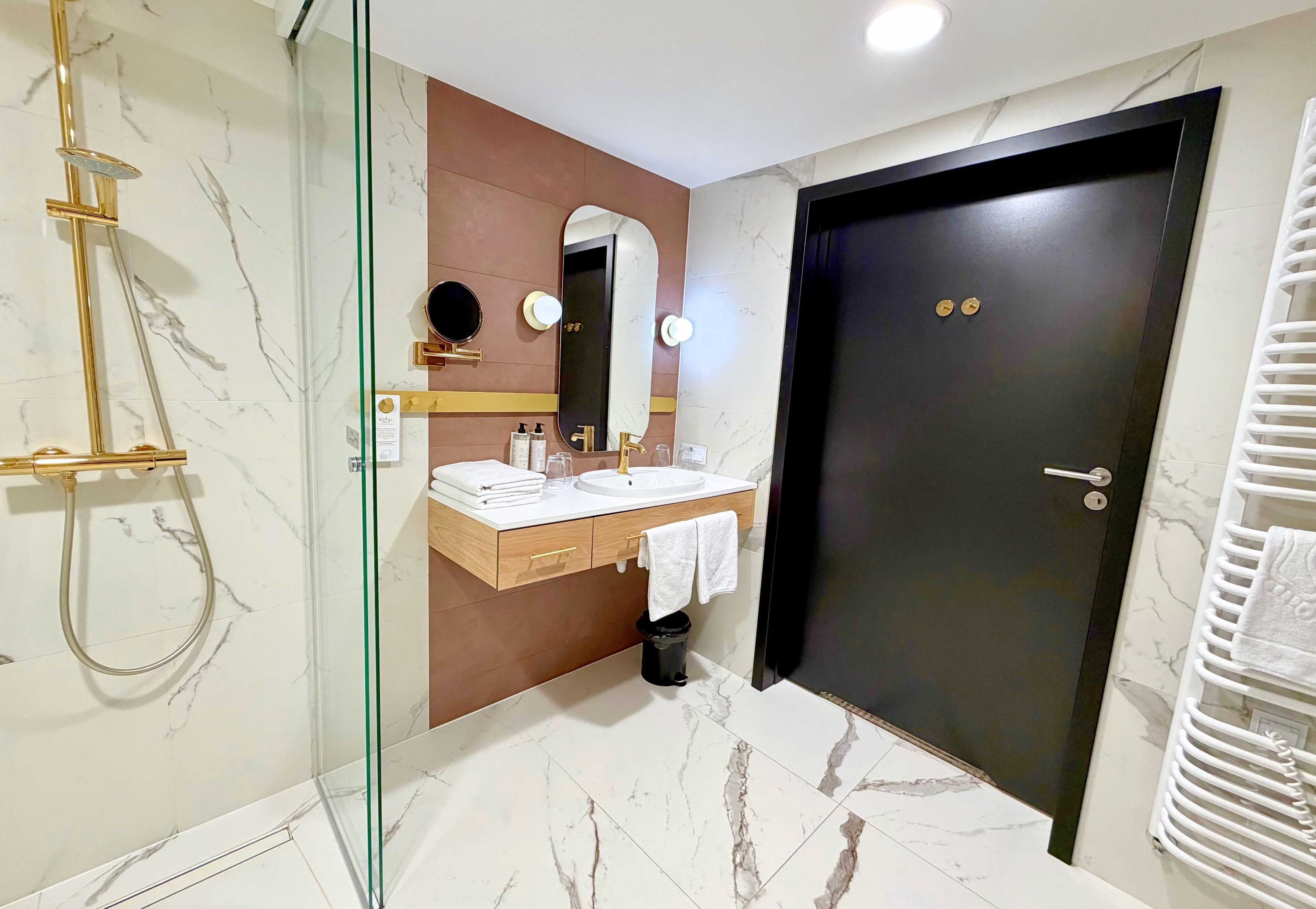 A modern bathroom with a glass-enclosed shower, a vanity with a mirror, and a dark door.