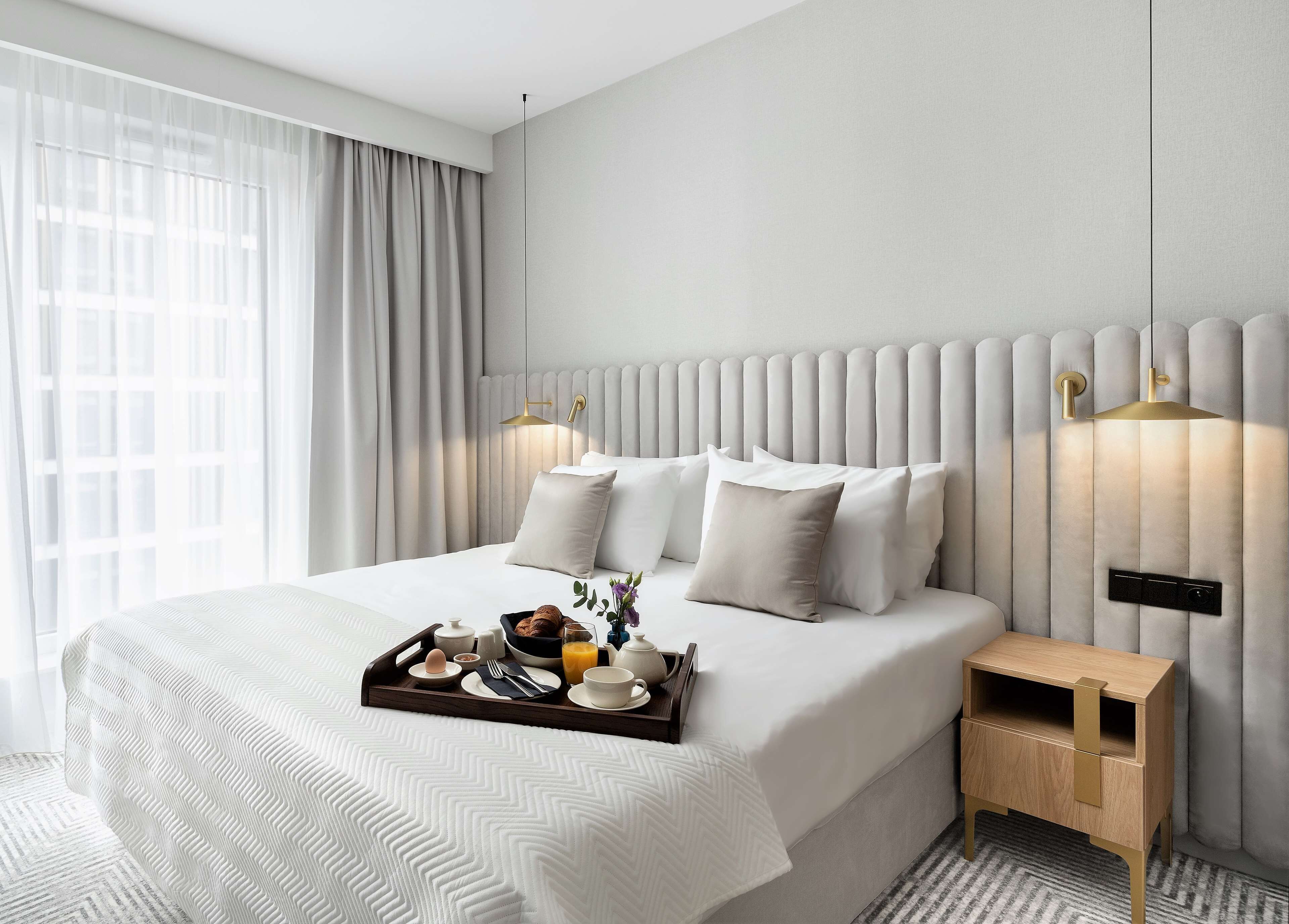 A modern hotel room with a large bed, a bedside table, and a tray with breakfast items.