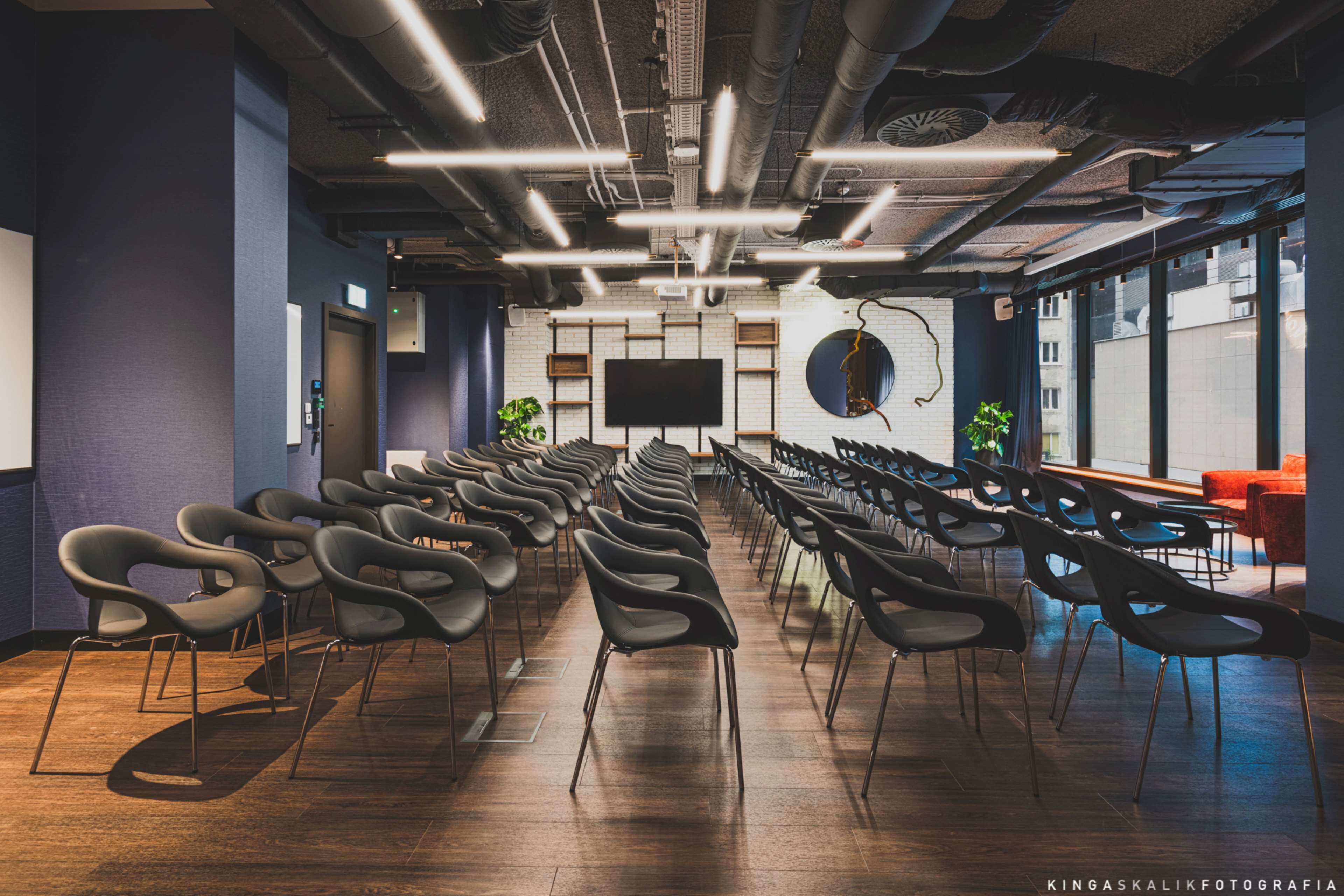 A conference room with rows of chairs, a large screen, and a plant.