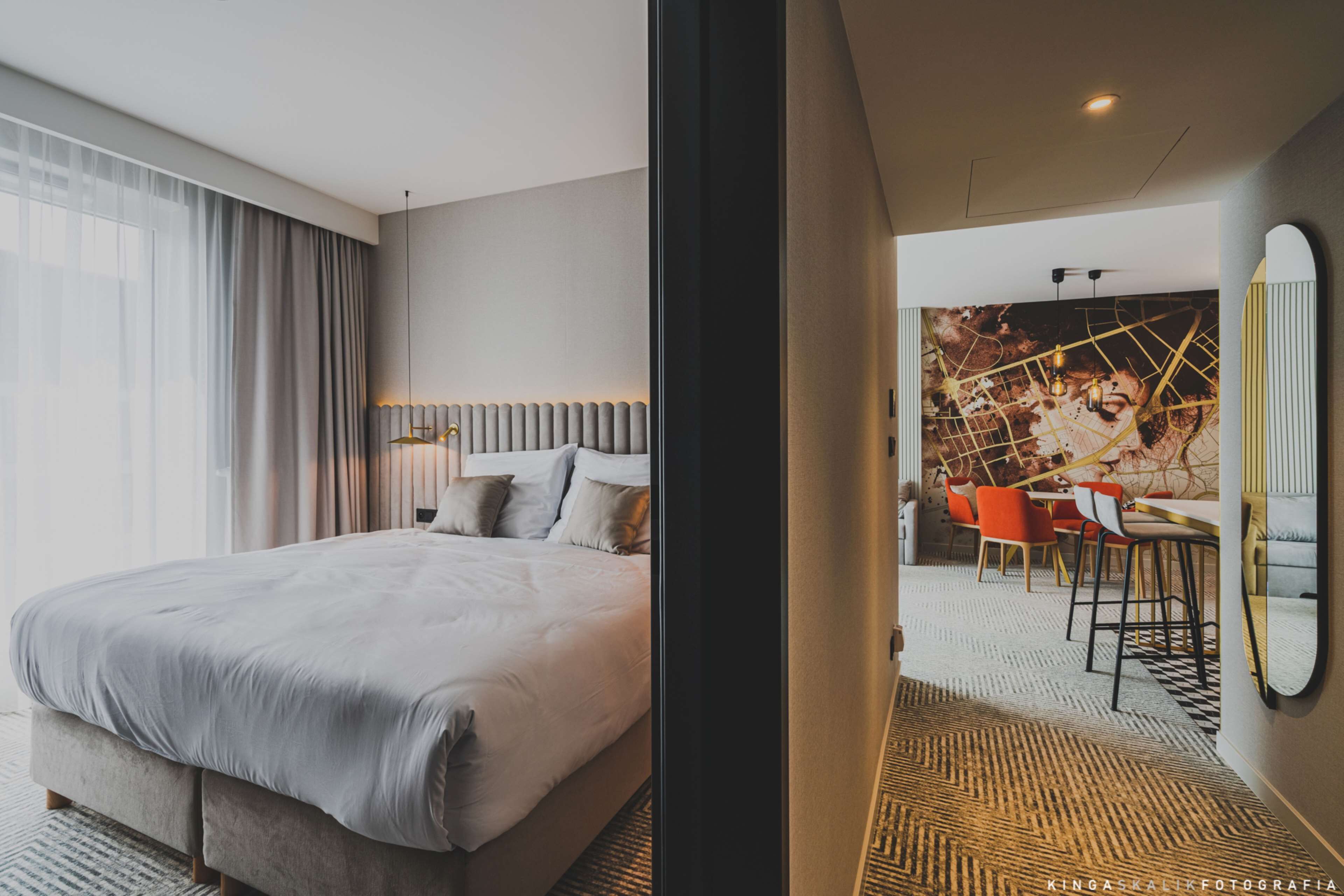 A modern hotel room with a large bed, a dining area with a table and chairs, and a large mirror on the wall.