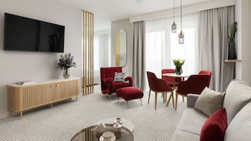 A modern living room with a sofa, red chairs, a wooden console, a TV, and a dining area with a table and chairs.