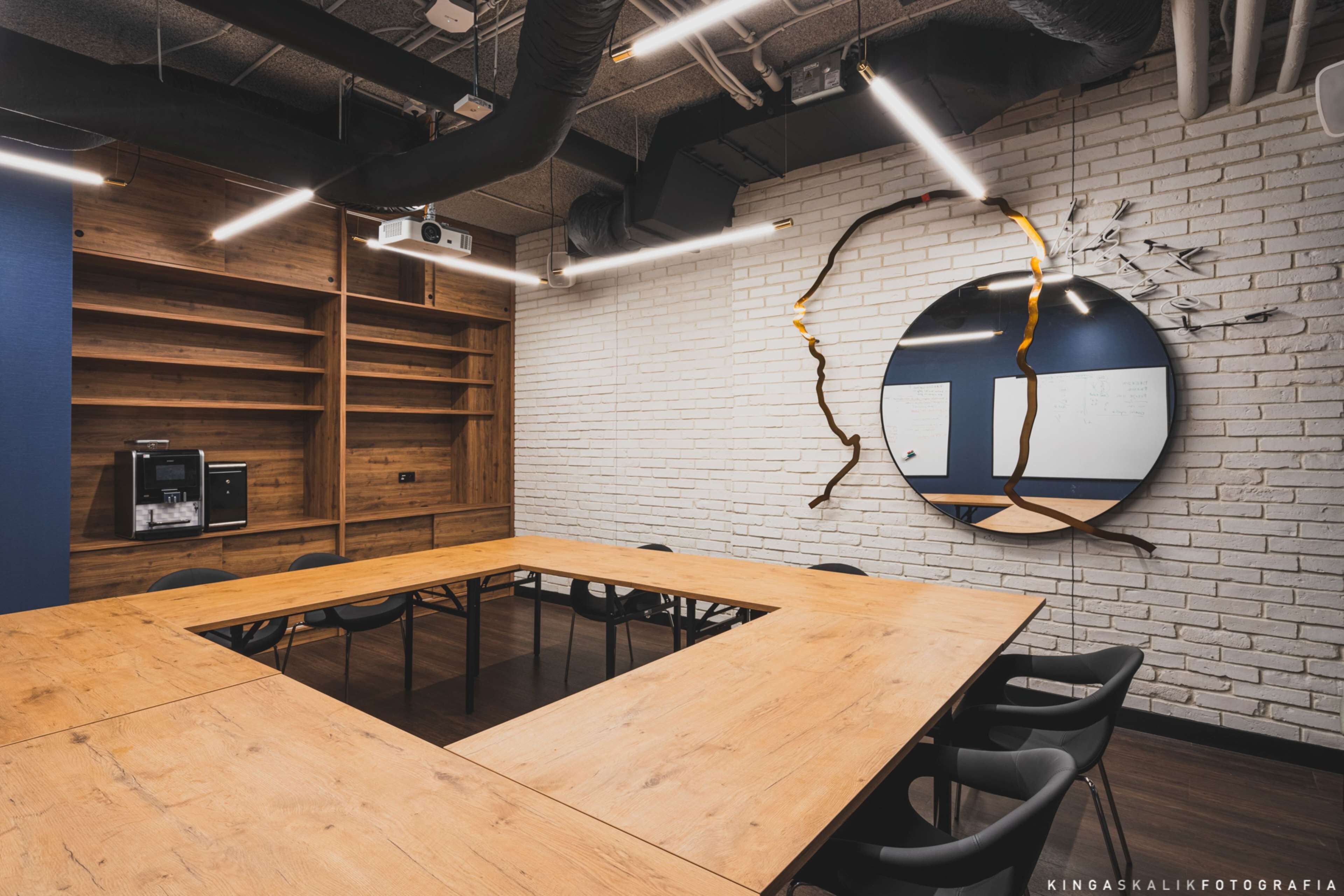 A conference room with a long wooden table, black chairs, a white brick wall, and a circular wall decoration.