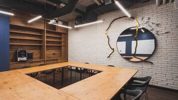 Une salle de conférence avec une longue table en bois, des chaises noires, un mur en briques blanches et un élément décoratif circulaire sur le mur.