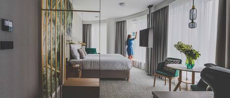 A modern hotel room with a large bed, a desk, a chair, and a TV.